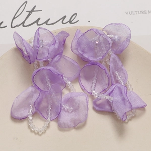 Close-up of lavender organza petal earrings with crystal beaded tassel on a neutral dish
