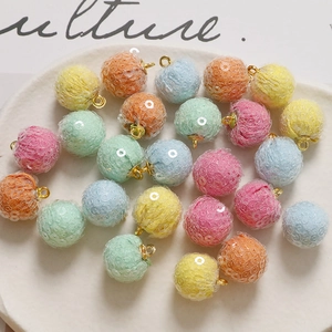 Macro shot of colorful mesh sequins pompom charms with golden loops on white plate