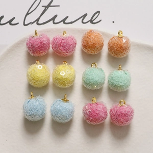 Macro view of 12 colorful glitter pompom charms with gold loops on a textured tray