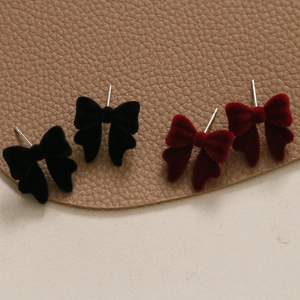 Détail de boucles d'oreilles nœuds en velours noir et rouge foncé sur cuir texturé