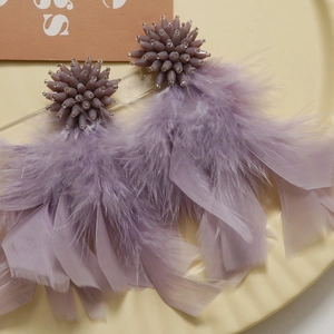 Detailed close-up of purple feather earrings with beaded sphere and silk ribbons