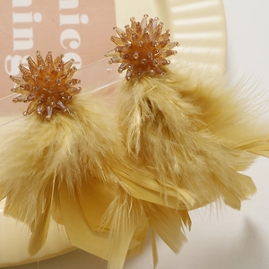 Close-up of handmade earrings with brown beads and long soft yellow feather fringe