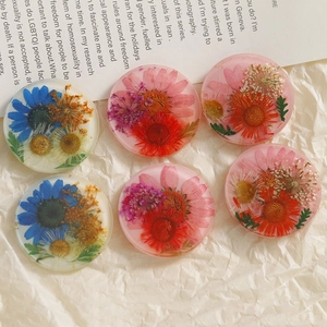 Flat lay of clear resin round pendants with real pressed flowers on vintage paper
