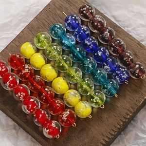 Dettaglio macro di perle di vetro colorate da 12mm con anelli in metallo dorato su legno scuro