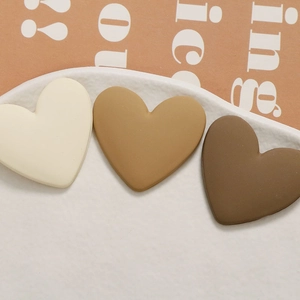 Three matte resin heart charms in earthy tones on a white ceramic plate for DIY crafts