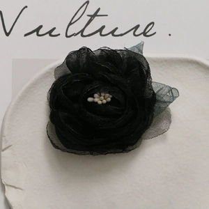 Detailed macro of a black mesh camellia flower brooch with pearl center and green leaves