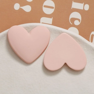Close-up of pink matte heart-shaped earrings on a white ceramic plate backdrop