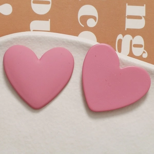 Macro shot of matte pink heart-shaped earrings on a white textured ceramic plate