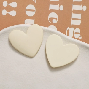 Macro close-up of cream matte heart-shaped resin stud earrings on white ceramic plate