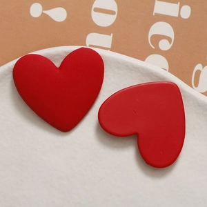 Detail of red matte heart-shaped resin stud earrings on a white textured plate