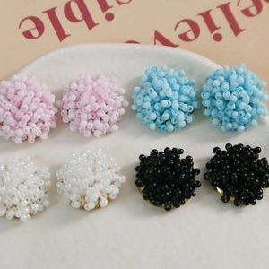 Macro detail of handmade beaded flower earrings in macaron pink, blue, white, and black