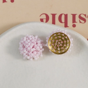 Pink macaron beaded flower earrings with gold textured base on a ceramic plate