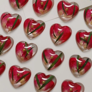 Macro detail of heart resin charms with real dried red flowers and golden beads inside