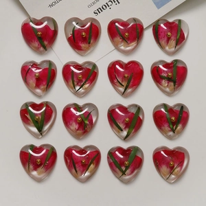 Flat lay of 16 heart-shaped resin charms with embedded real red dried flowers and green leaves