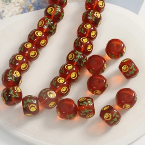 Macro view of 14mm red resin beads with painted smiley faces and green leaves for DIY jewelry