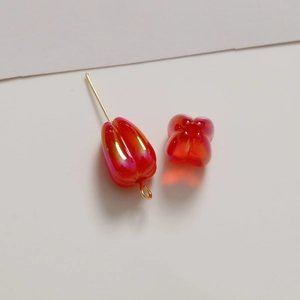 Macro detail of red tulip-shaped acrylic beads with iridescent finish and gold metal pins