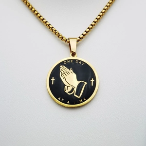 Detailansicht eines goldenen Gebetshände Anhängers mit ONE DAY AT A TIME Text