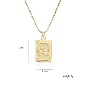 Detalle de colgante rectangular dorado con letra A y textura de rayos solares con cadena