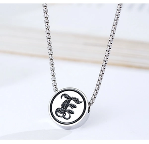 Detailed macro of a silver round pendant featuring a gothic letter E with floral patterns