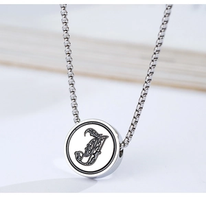 Macro shot of polished stainless steel round pendant featuring engraved letter J detailing