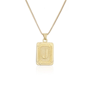 Detalle del colgante rectangular dorado con letra J grabada y cadena de caja en acero titanio