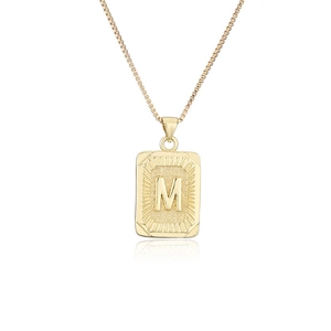 Detalle de colgante rectangular dorado con letra M en relieve en una cadena de caja