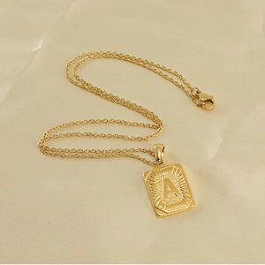 Détail du pendentif rectangulaire plaqué or 18K avec lettre A gravée sur tissu satiné