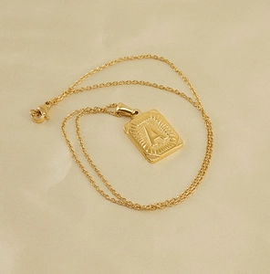 Détail macro d'un pendentif carré plaqué or 18 carats avec lettre A en relief et texture rayon