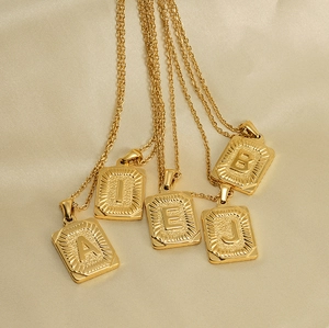 Detailed macro of gold 18K square letter pendants showing textured radiant engraved patterns