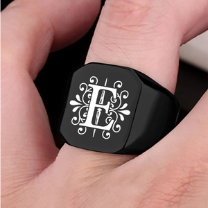 Close-up of black square signet ring featuring a white floral letter E on male finger