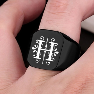 Detail of a black square stainless steel ring featuring a decorative letter H engraving