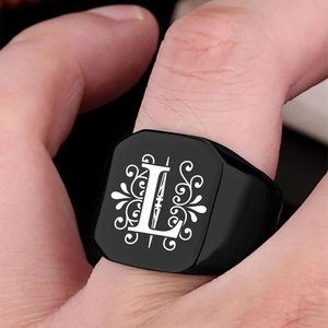 Detailed close-up of a black signet ring with a white Gothic letter L on the index finger