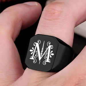 Detail of black stainless steel signet ring featuring a white engraved letter M and scrolls