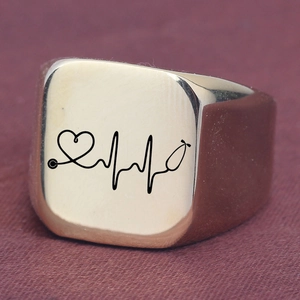 Macro detail of gold signet ring featuring engraved heartbeat and stethoscope medical motif