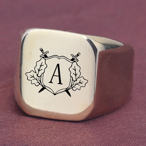 Gold signet ring with engraved shield, crossed swords, and initial A on purple fabric