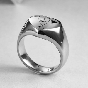 Detalle macro de un anillo ancho plateado con grabado de corazón y la palabra Love