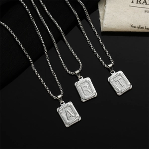 Macro detail of silver rectangle initial pendant necklaces on a dark textured background