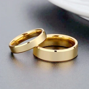 Macro shot of two polished gold rings with beveled edges on a textured grey surface