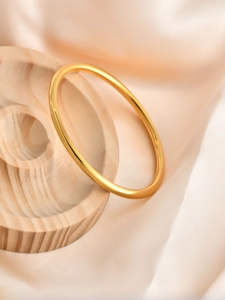 Close-up of polished 6mm gold-tone solid bangle resting on a wooden display stand