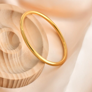 Polished golden solid minimalist bangle displayed on elegant silk background and wood stand