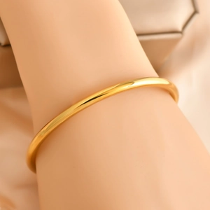 Minimalist 6mm gold polished solid bangle on a model wrist with soft warm lighting