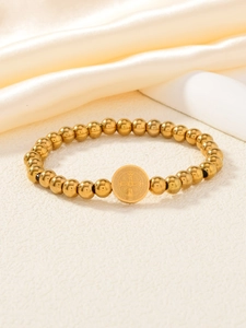 Détail d'un bracelet à billes dorées avec un pendentif religieux de la médaille Saint-Benoît