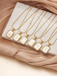 Detail von Goldketten mit Buchstaben, weißer Muschel und Zirkonia auf Seidenstoff