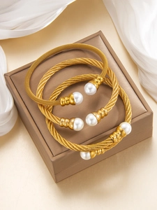 Dettaglio di bracciali in cavo d'acciaio placcati oro 18K con eleganti perle bianche