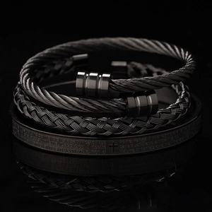 Detail of gunmetal braided cable bracelets and cross engraved cuff on reflective surface