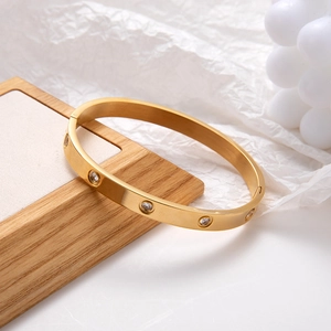 Polished gold stainless steel bangle with inlaid crystals on a wooden display