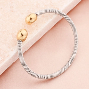 Twisted cable cuff bracelet with silver wire and gold-tone spherical end caps on marble