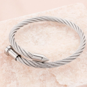 Silver stainless steel nail twisted wire bangle displayed on a pink textured stone