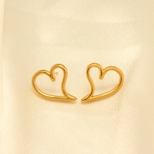 Detalle de los pendientes de corazón hueco irregular en oro sobre tela de seda champán