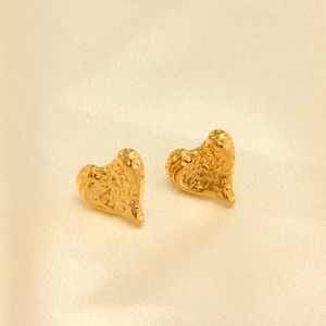 Detalle de pendientes de corazón en oro 18k con textura martillada sobre seda